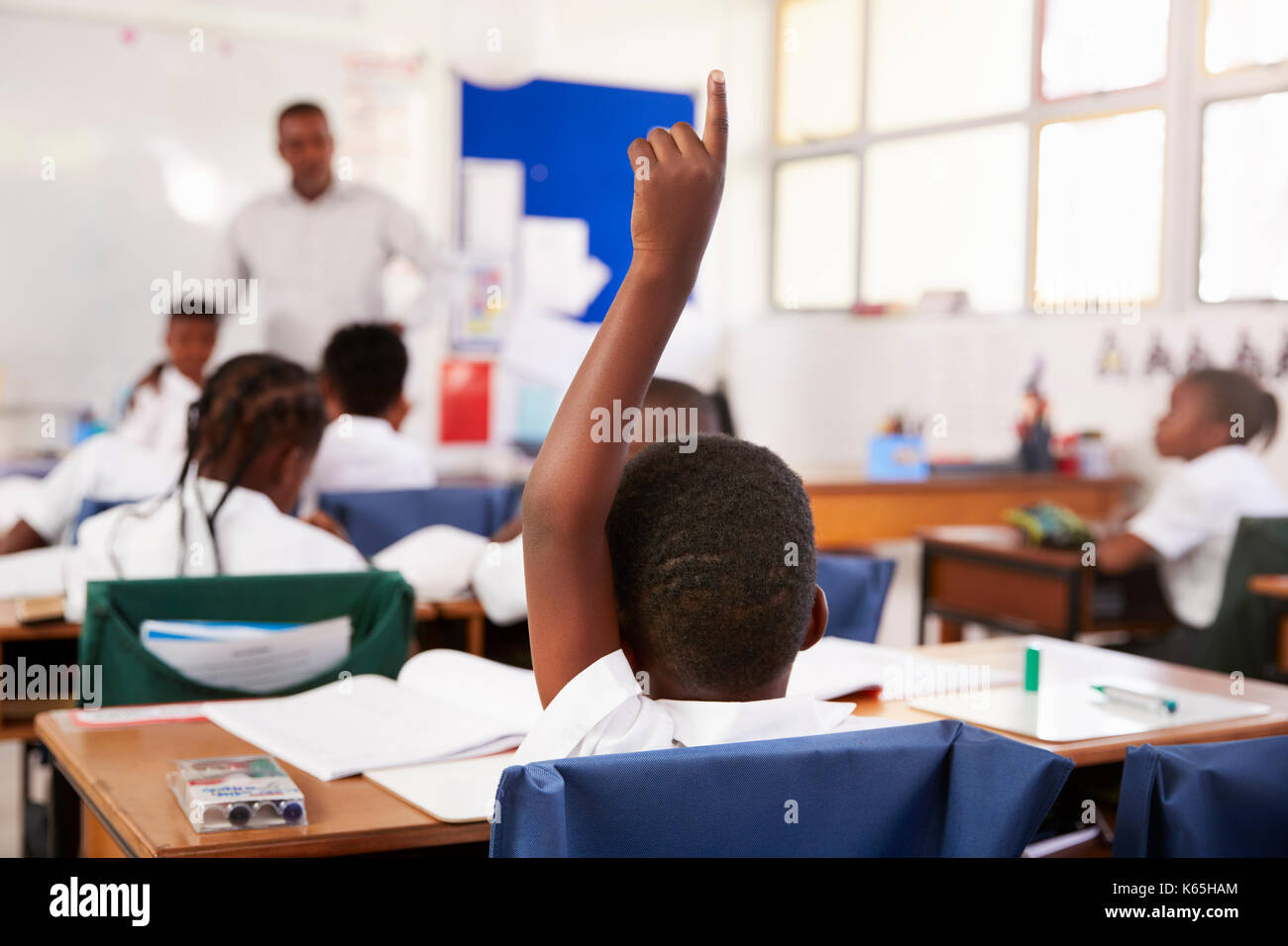 Bambino alzando la mano per rispondere in una scuola elementare lezione Foto Stock