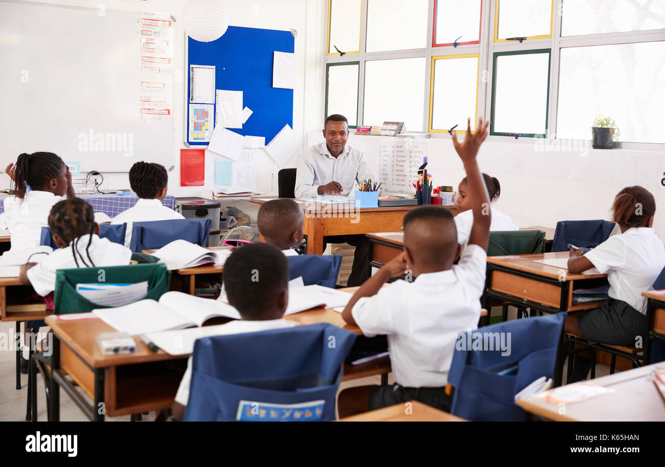 Bambino alzando la mano per insegnante in una scuola elementare di classe Foto Stock