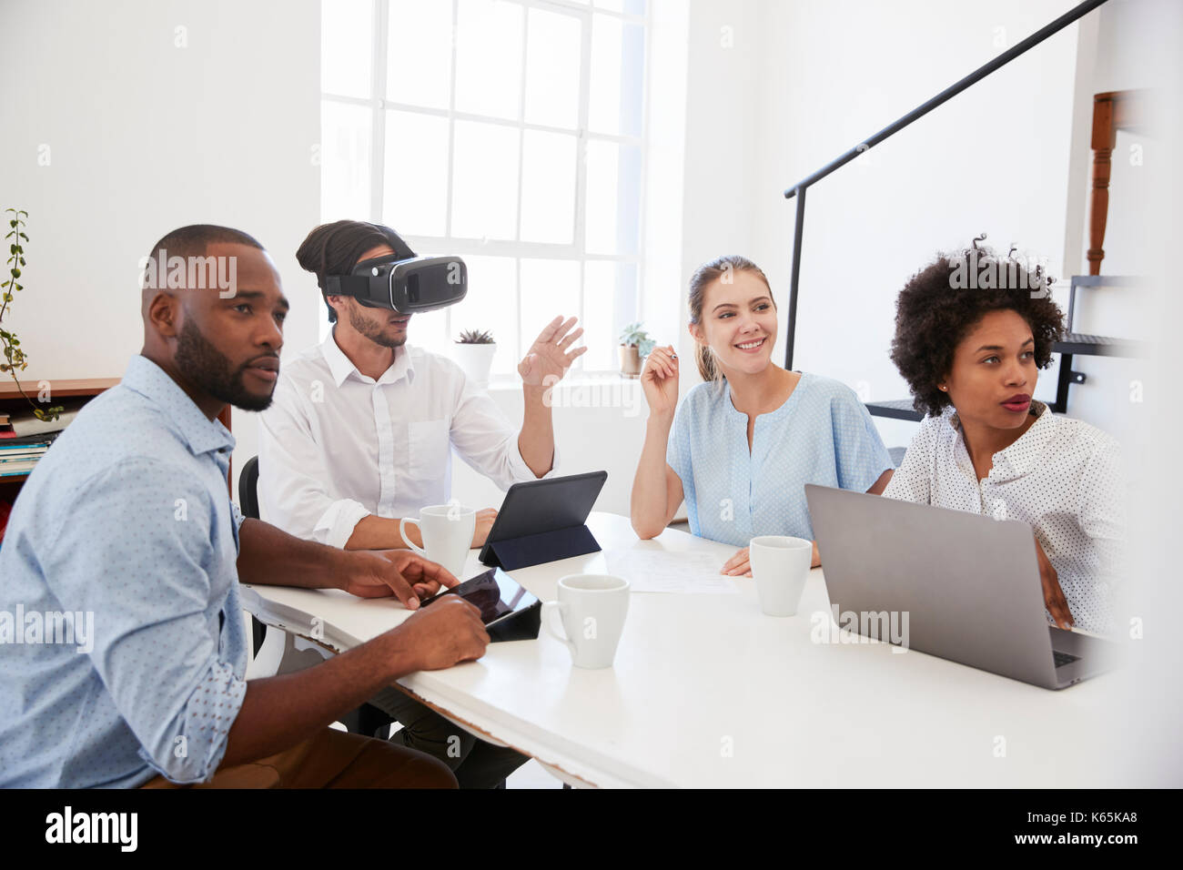 Uomo in occhiali VR a una scrivania con i colleghi in un ufficio Foto Stock