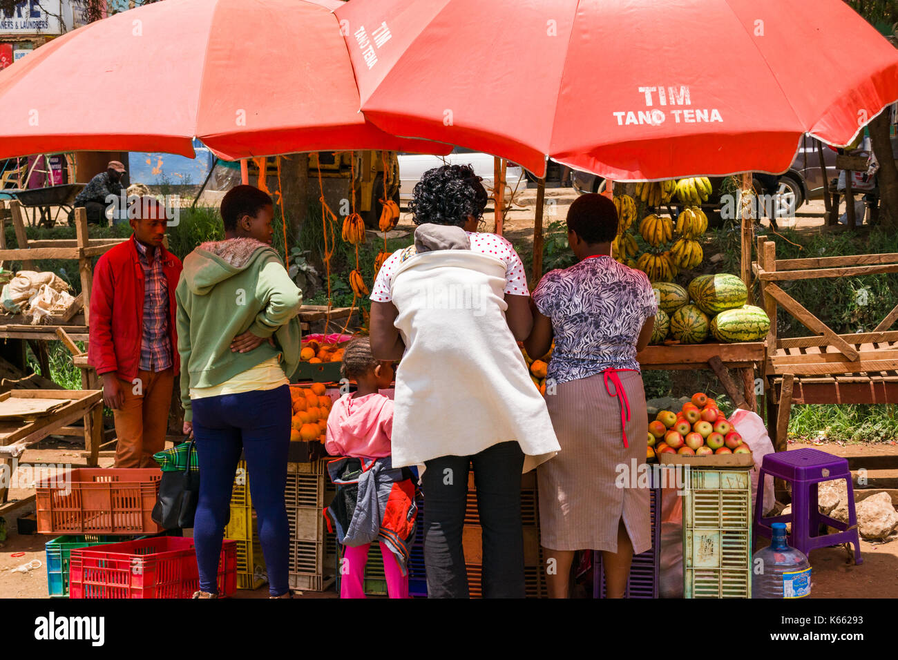 Le bancarelle del mercato in ombra sotto gli ombrelloni per la vendita di frutta e verdura come persone stand browsing, Kenya Foto Stock