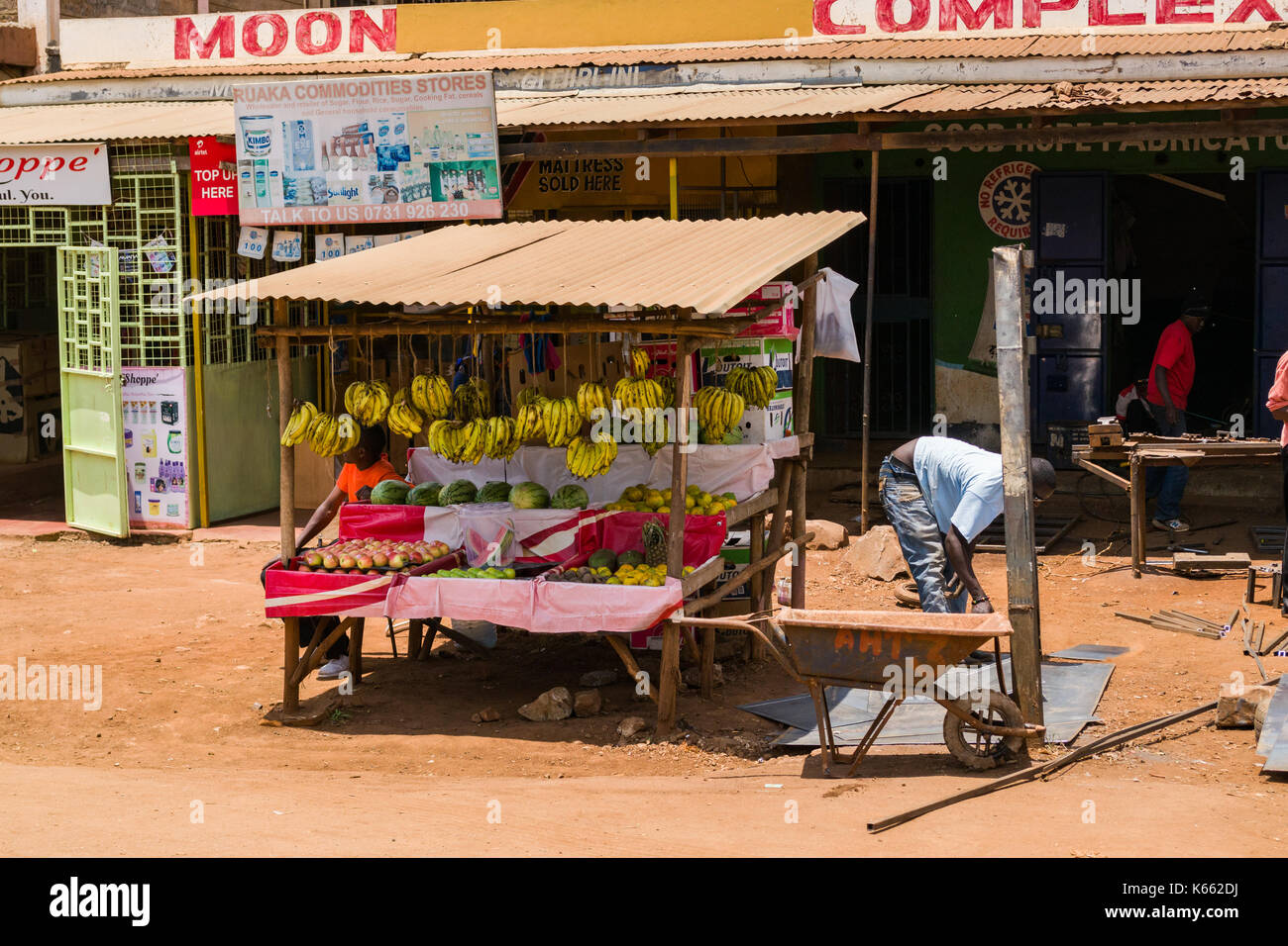 Piccolo mercato stallo con la frutta e la verdura per la vendita di fronte a negozi, Kenya Foto Stock