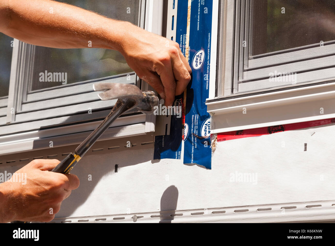 Un lavoratore edile martellare un chiodo per fissare la striscia di vinile in una finestra in Ontario, Canada. Foto Stock