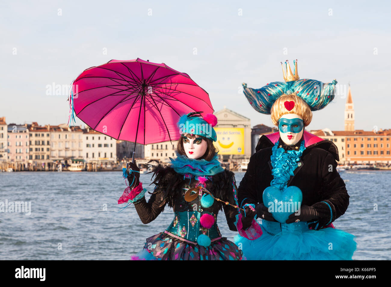Il Carnevale di Venezia 2017, Veneto, Italia, colorato matura in costumi e masksposing di fronte alla laguna con il Castello dello skyline della città dietro di loro Foto Stock