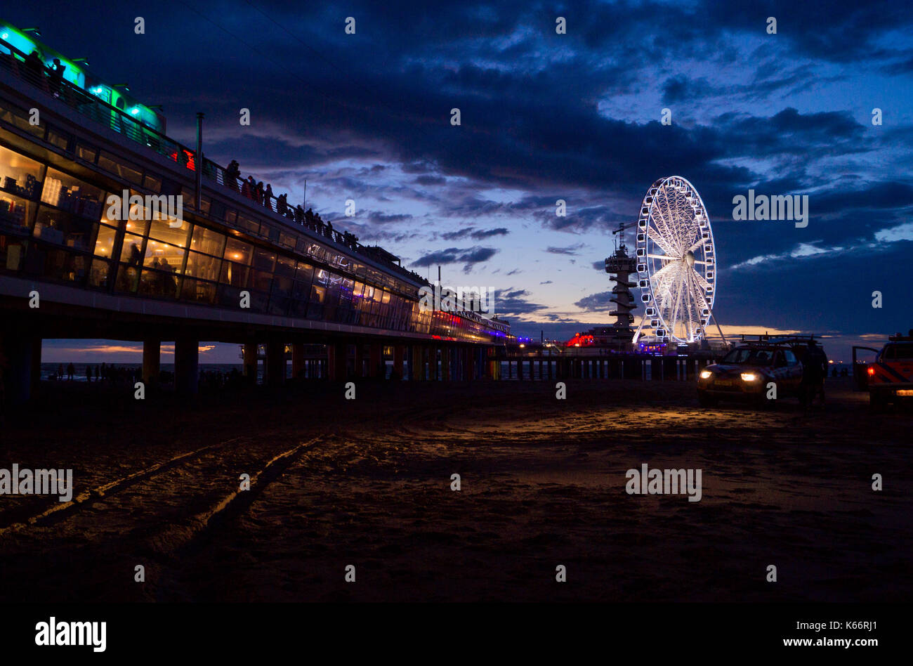 Il molo presso la spiaggia di Scheveningen, Paesi Bassi durante la notte con la ruota panoramica Ferris illuminato con luci in background al crepuscolo/tramonto Foto Stock