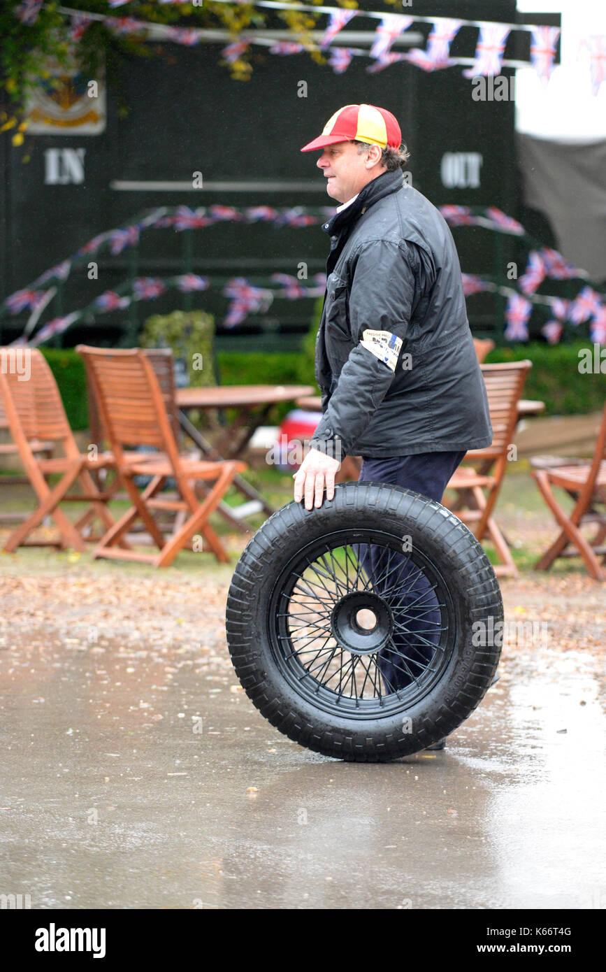 Un membro dell'equipaggio dei box tira una ruota di scorta dai box al Goodwood Revival 2017. Piove Foto Stock