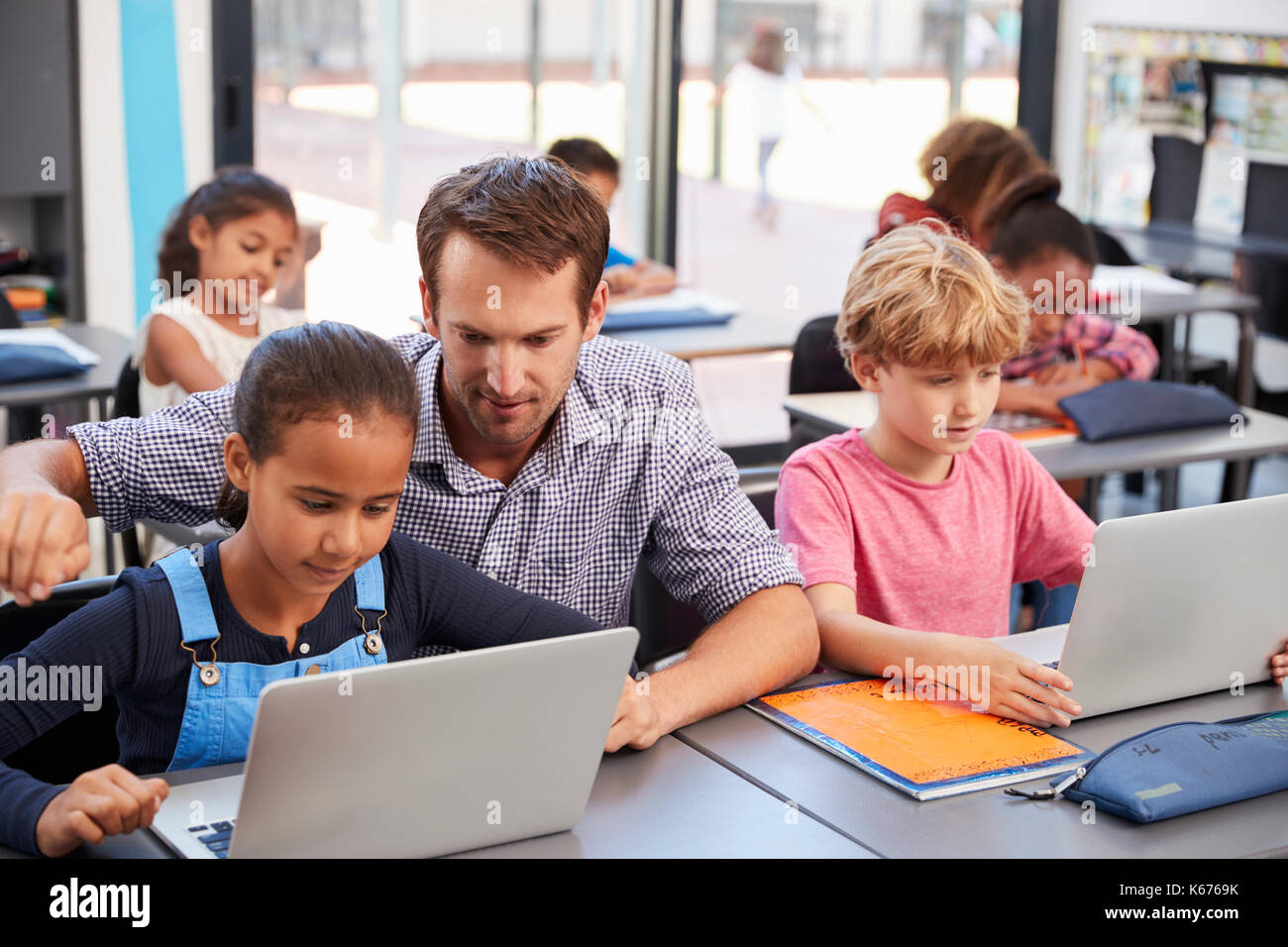 Insegnante aiutando i giovani studenti utilizzano i computer portatili in classe Foto Stock