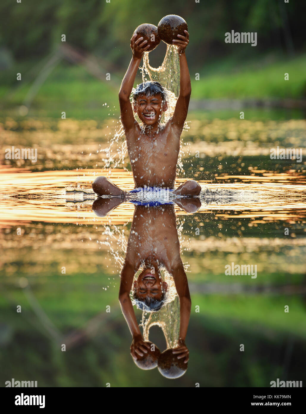 Ragazzo seduto in un fiume versando acqua sopra la sua testa, Thailandia Foto Stock