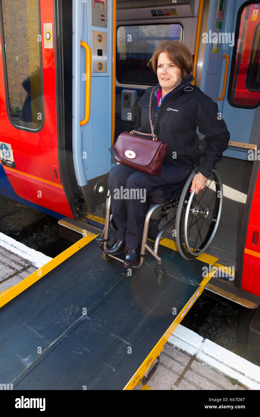 Sedia a rotelle utente / persona in una sedia a rotelle in partenza / lasciando / scendere dal treno di un carrello su una piattaforma tramite una rampa previste in corrispondenza della stazione. Foto Stock