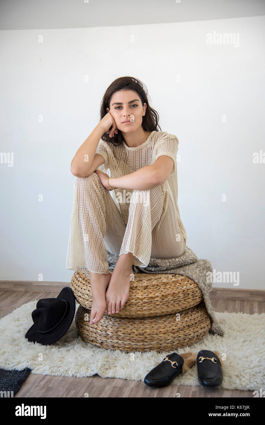 Giovane donna seduta da sola in un pouf in camera sua e guardando la telecamera. Foto Stock
