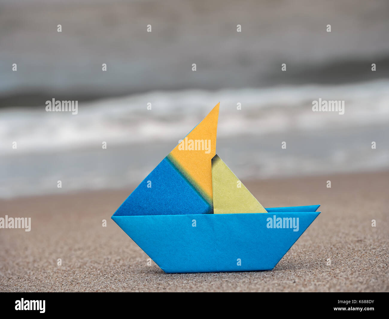 Blu e Giallo barca di carta sulla spiaggia di sabbia contro il mare Foto Stock