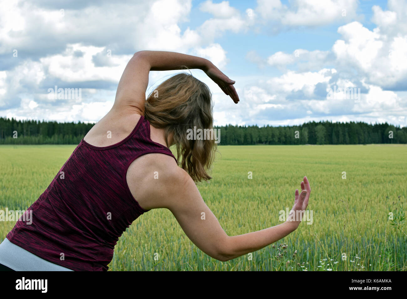 Di mezza età donna yoga stretching e di esercizio all'esterno. vista posteriore del campo sullo sfondo. Foto Stock