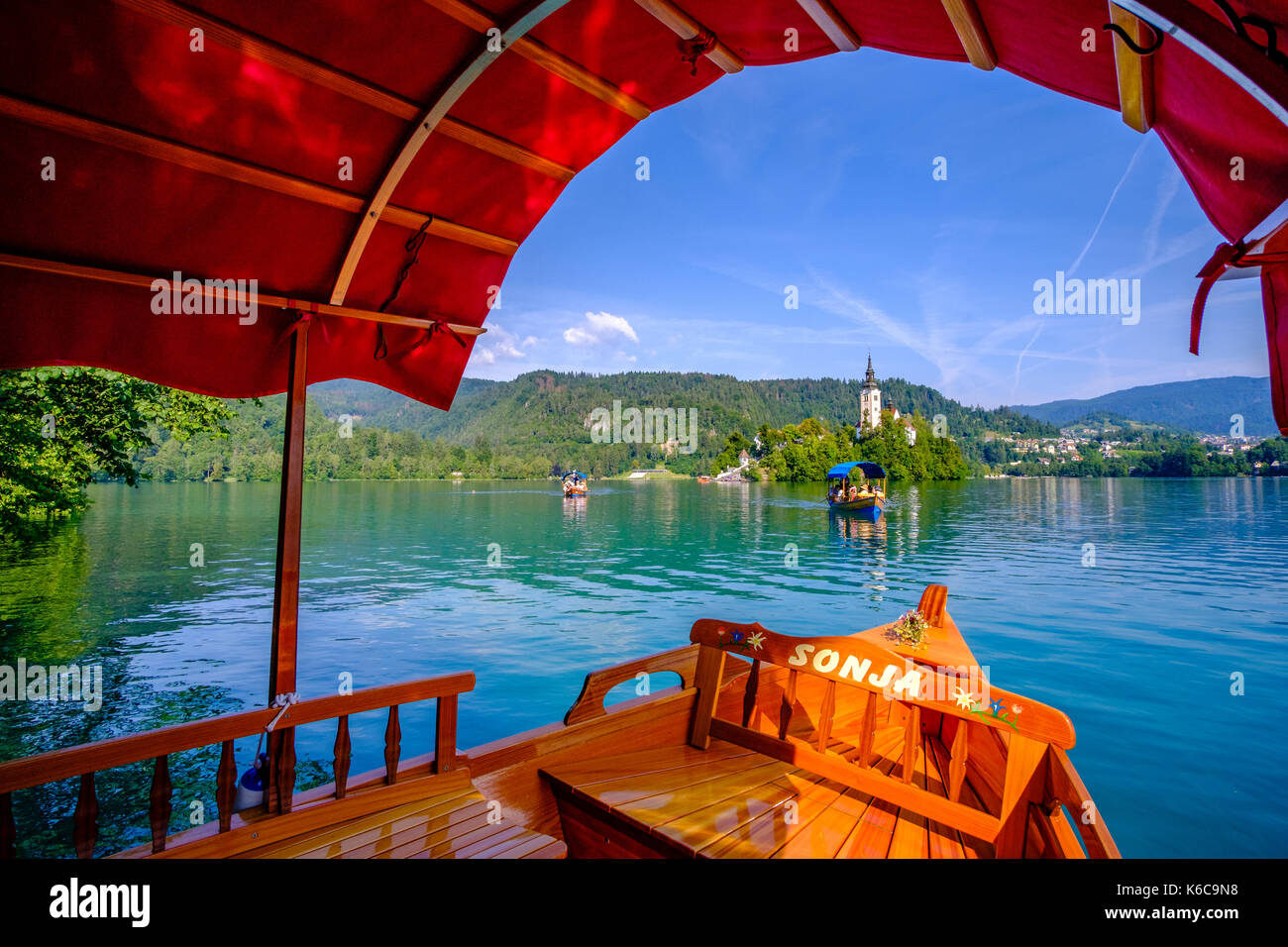 I turisti in una imbarcazione proveniente dall isola di Bled, Blejski Otok, con la chiesa di pellegrinaggio dedicata all Assunzione di Maria si vede attraverso il lago di Bled e blejsk Foto Stock