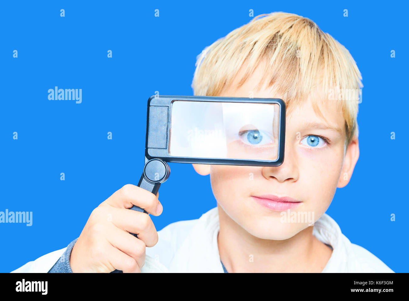 Ritratto di bambino giovane ragazzo biondo con lente di ingrandimento. concetto di scienziato pazzo. isolato sul blu sullo sfondo di calettamento. Foto Stock