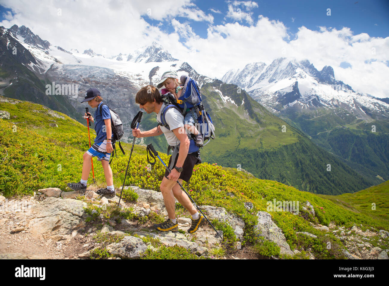 Padre escursioni in montagna con due figli con uno sulla sua schiena, Chamonix, Alta Savoia, Francia Foto Stock