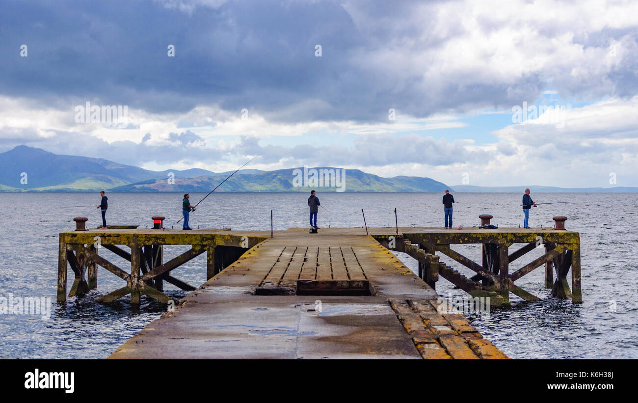 5 maschi la pesca alla fine del molo abbandonato a portencross, North Ayrshire, in Scozia in un giorno nuvoloso con l'isola di Arran all'orizzonte Foto Stock