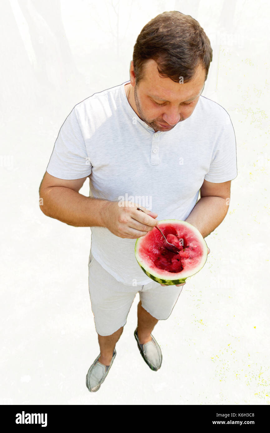 Uomo di mangiare una cucchiaiata di cocomero, scorcio dal di sopra, caricatura, isolati su sfondo bianco. Foto Stock