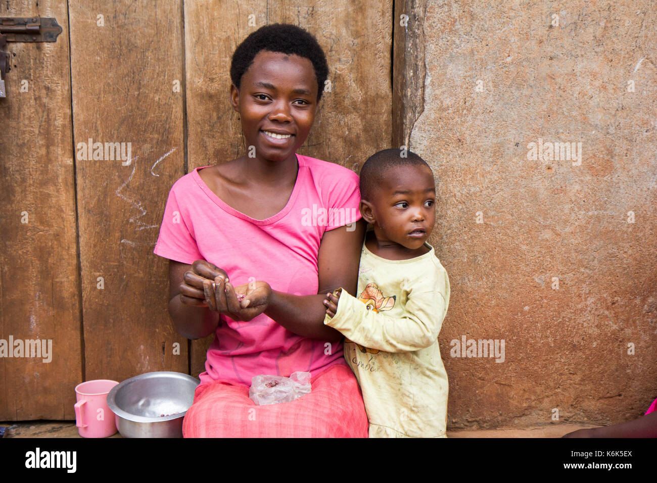 Lugazi, Uganda. 09 giugno 2017. Un ridere madre africana con un piccolo bambino ragazzo. la donna è seduta sulla soglia della porta grani di smistamento. Foto Stock