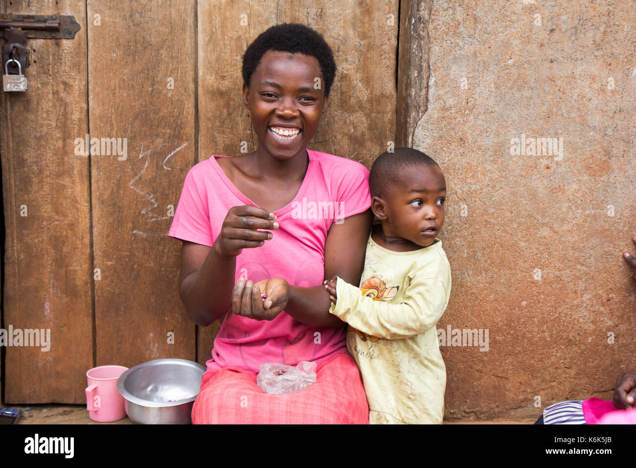 Lugazi, Uganda. 09 giugno 2017. Un ridere madre africana con un piccolo bambino ragazzo. la donna è seduta sulla soglia della porta grani di smistamento. Foto Stock