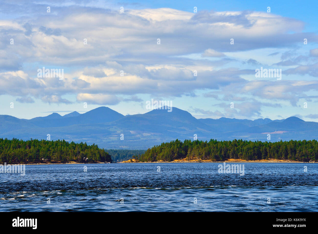 Un paesaggio orizzontale dell'Isola di Vancouver che guarda indietro verso le montagne boscose da una barca che viaggia nello stretto della Georgia sulla costa occidentale del British Columbia. Foto Stock