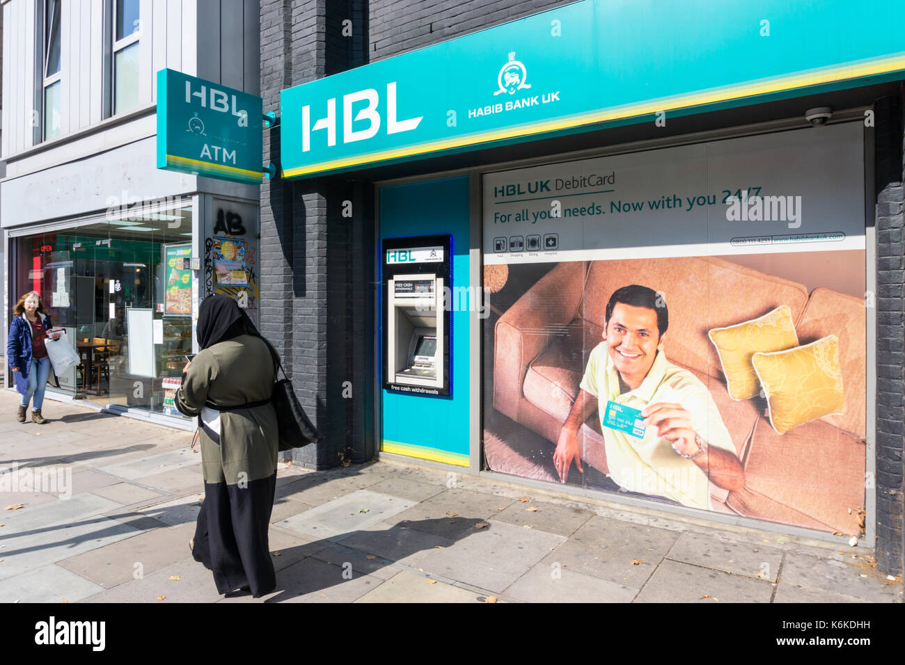 Una donna che indossa un hijab passeggiate passato un ramo del Pakistan in base Habib Bank UK e HBL ATM in Whitechapel Road, Londra. Foto Stock
