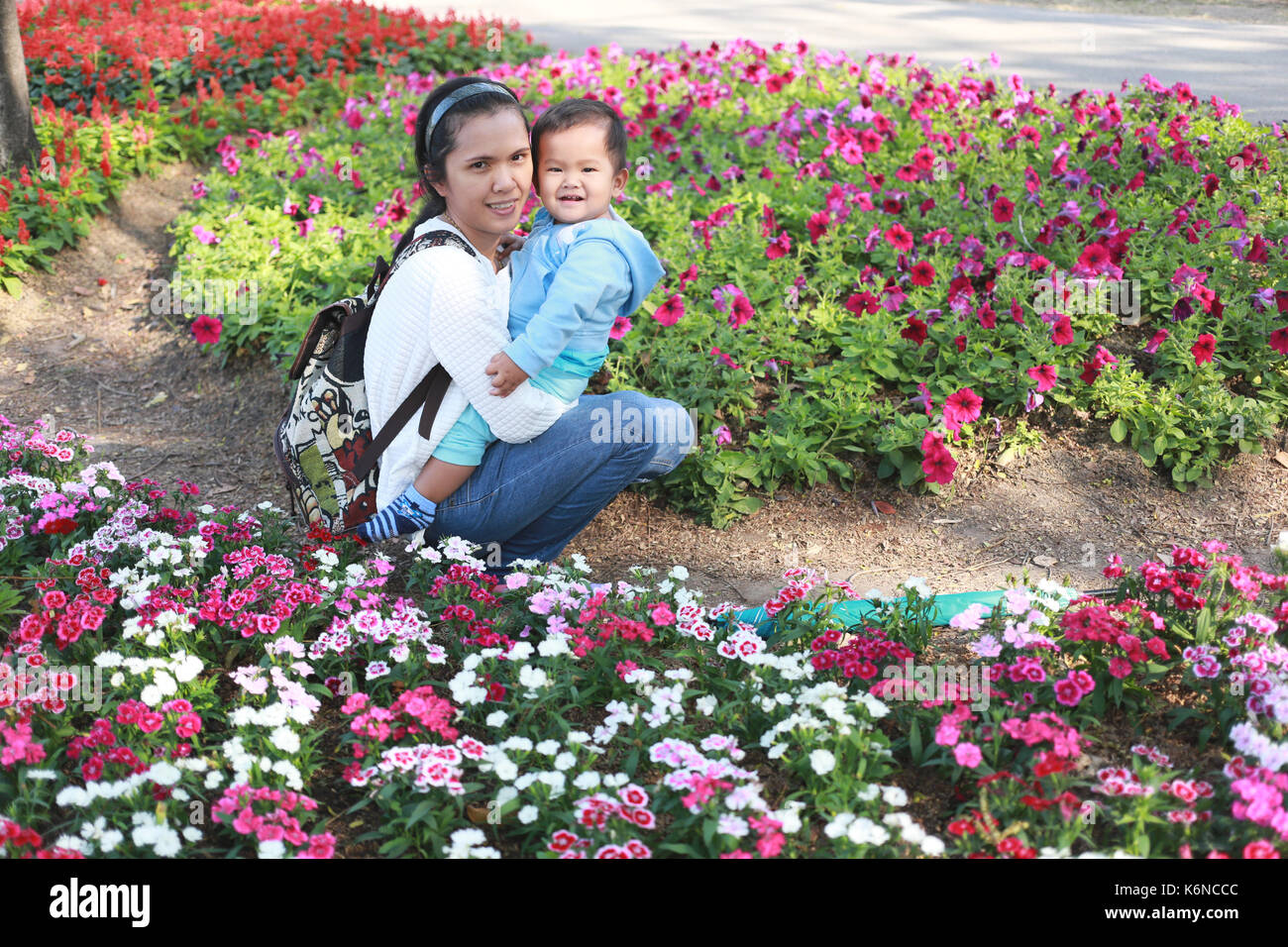 Ragazzo asiatico è felicemente nelle braccia della madre nel giardino dei fiori,concetto di amore e salute del bambino. Foto Stock