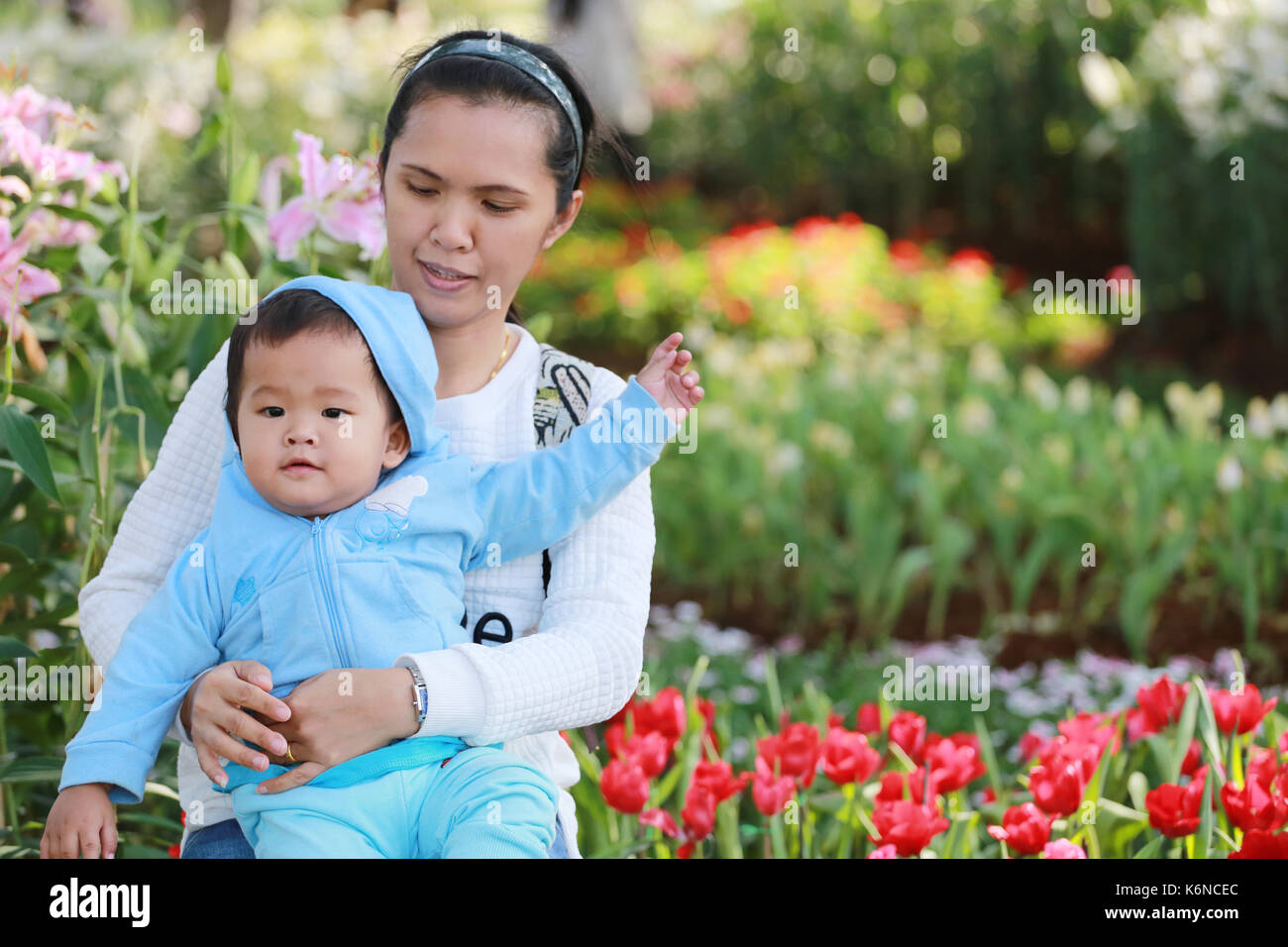 Ragazzo asiatico è felicemente nelle braccia della madre nel giardino dei fiori,concetto di amore e salute del bambino. Foto Stock