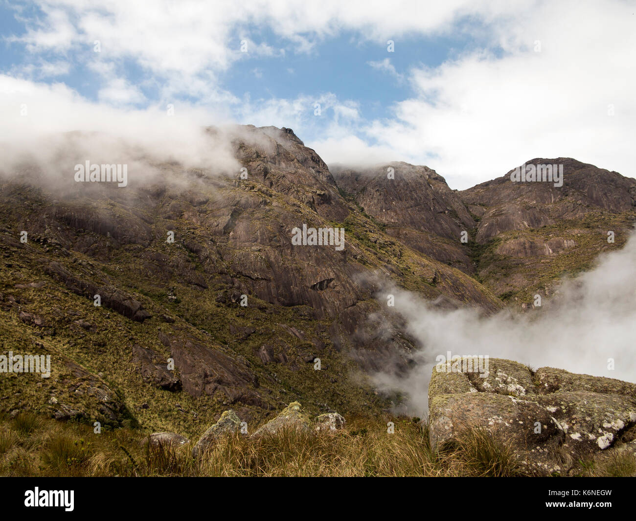 Roccia di una montagna con alcuni alberi e cespugli e una nuvola Foto Stock