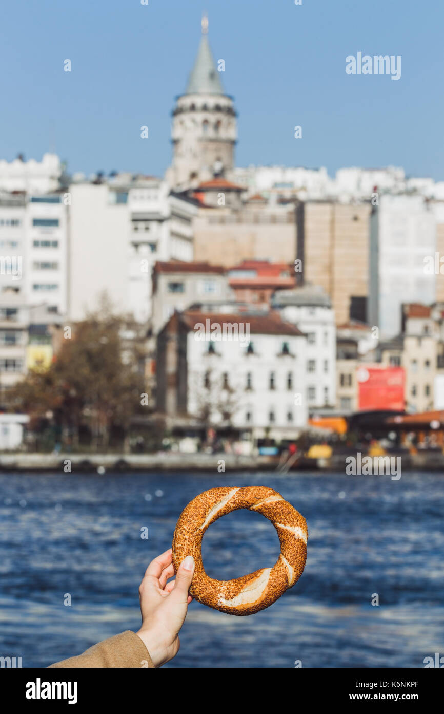 Donna mano che tiene un tradizionale bagno turco simit sul mare e sullo sfondo la torre di Galata Foto Stock