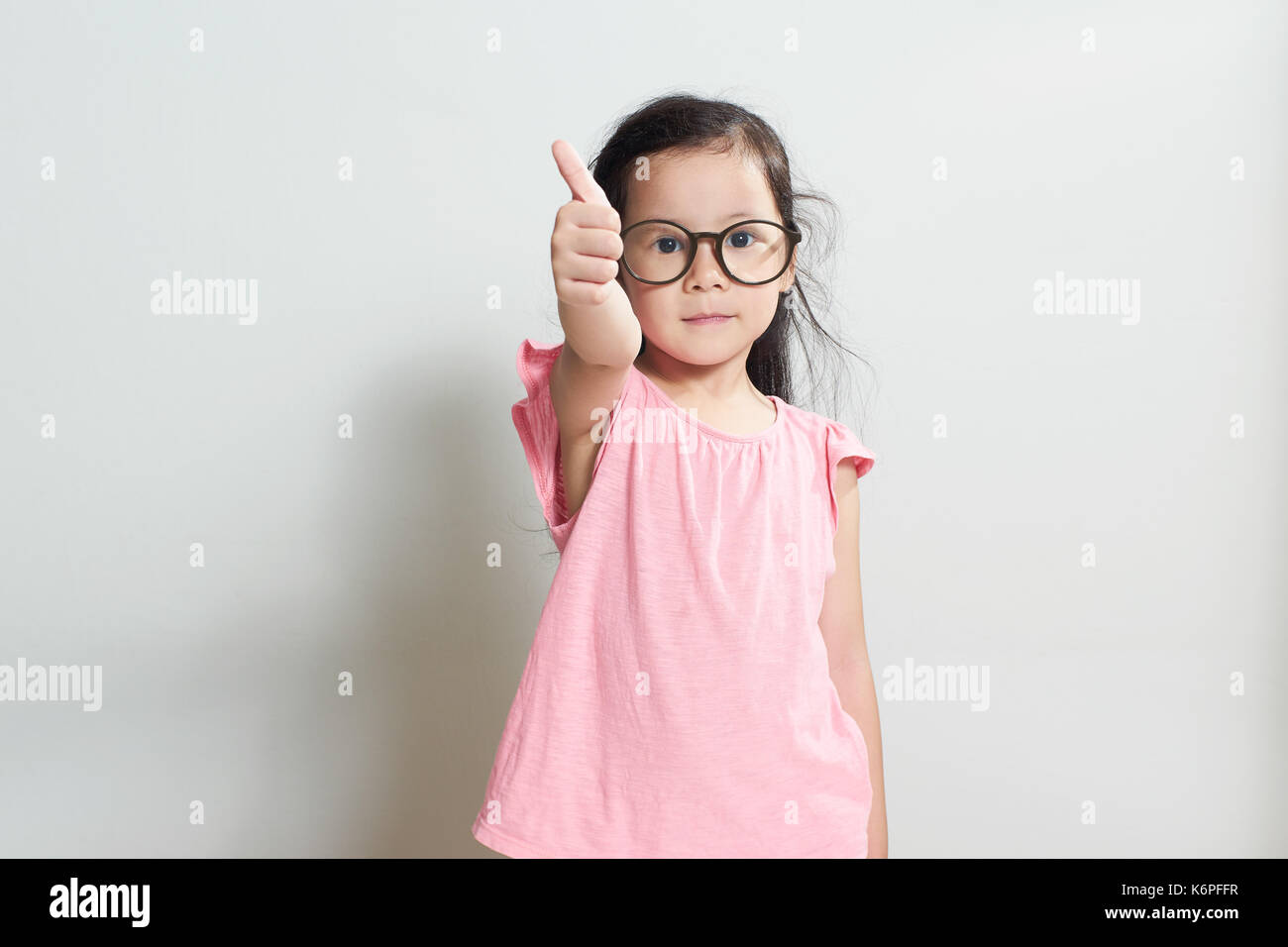 Bambina vestito in rosa è che mostra il pollice fino gesto , isolate su sfondo bianco . Foto Stock