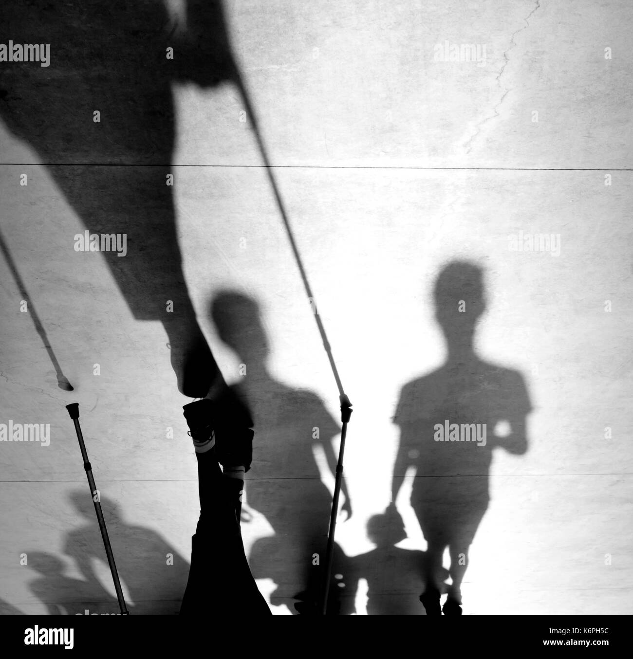Sfocata ombra silhouette di una persona anziana e camminare con i bastoncini nordic bastoni sul marciapiede e giovani a piedi dietro, in bianco e nero Foto Stock