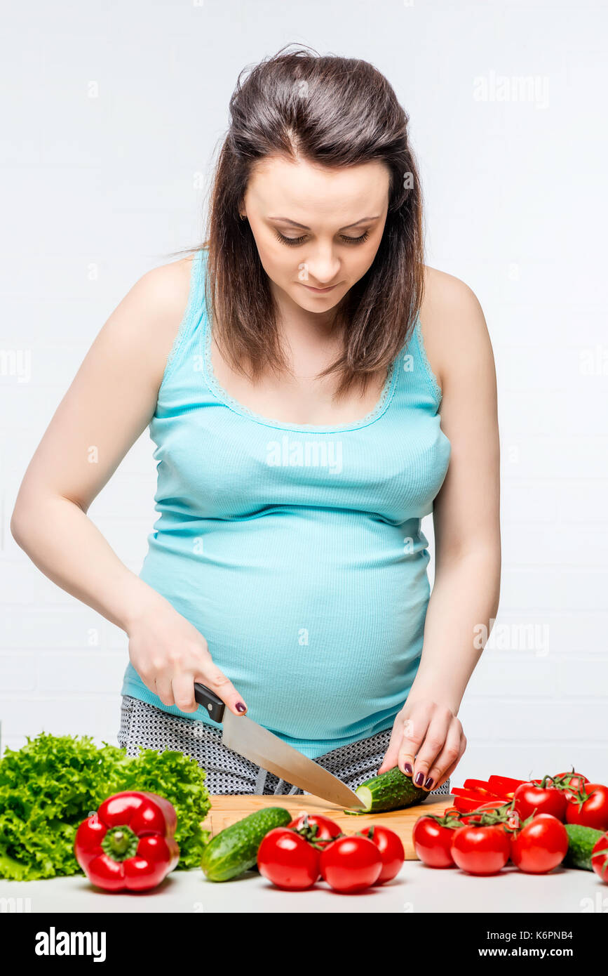 Ritratto verticale di una donna incinta durante la preparazione di una insalata di verdure Foto Stock