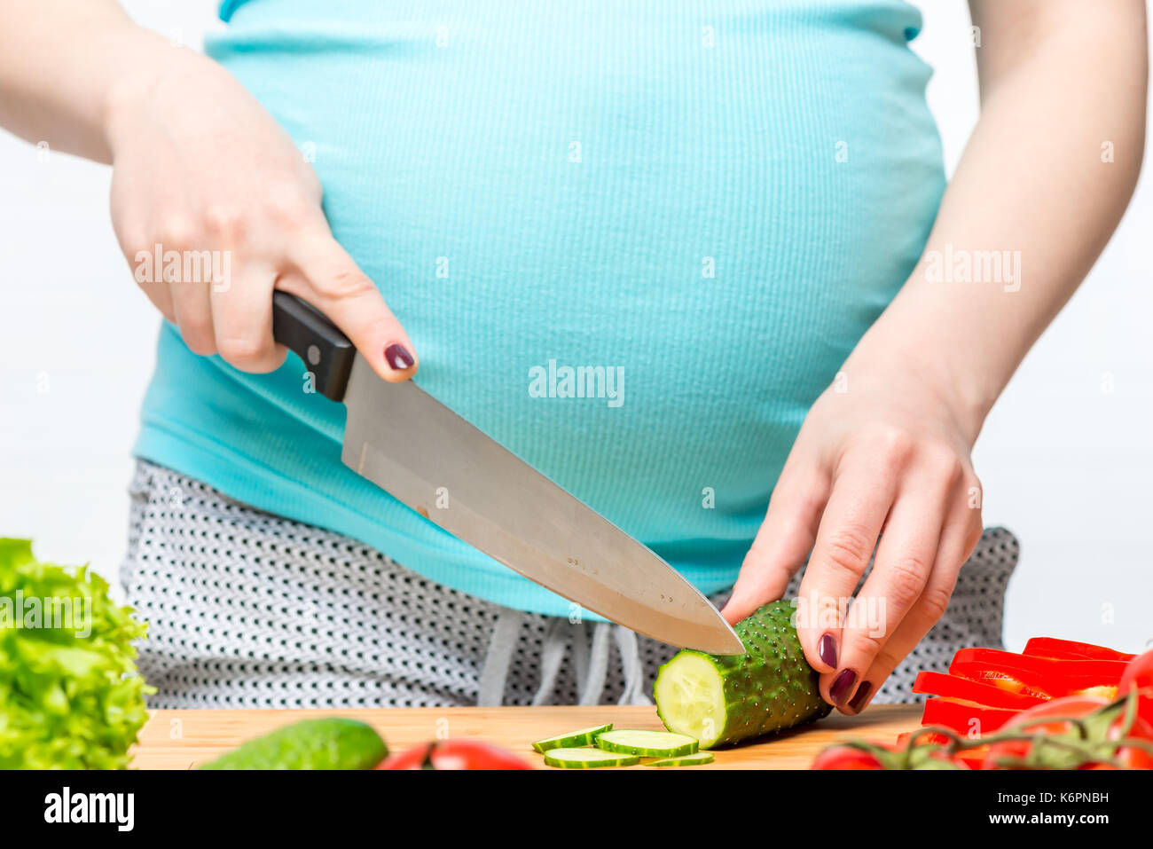 Giovane donna incinta con un coltello in mano si prepara un utile insalata, mani close-up Foto Stock