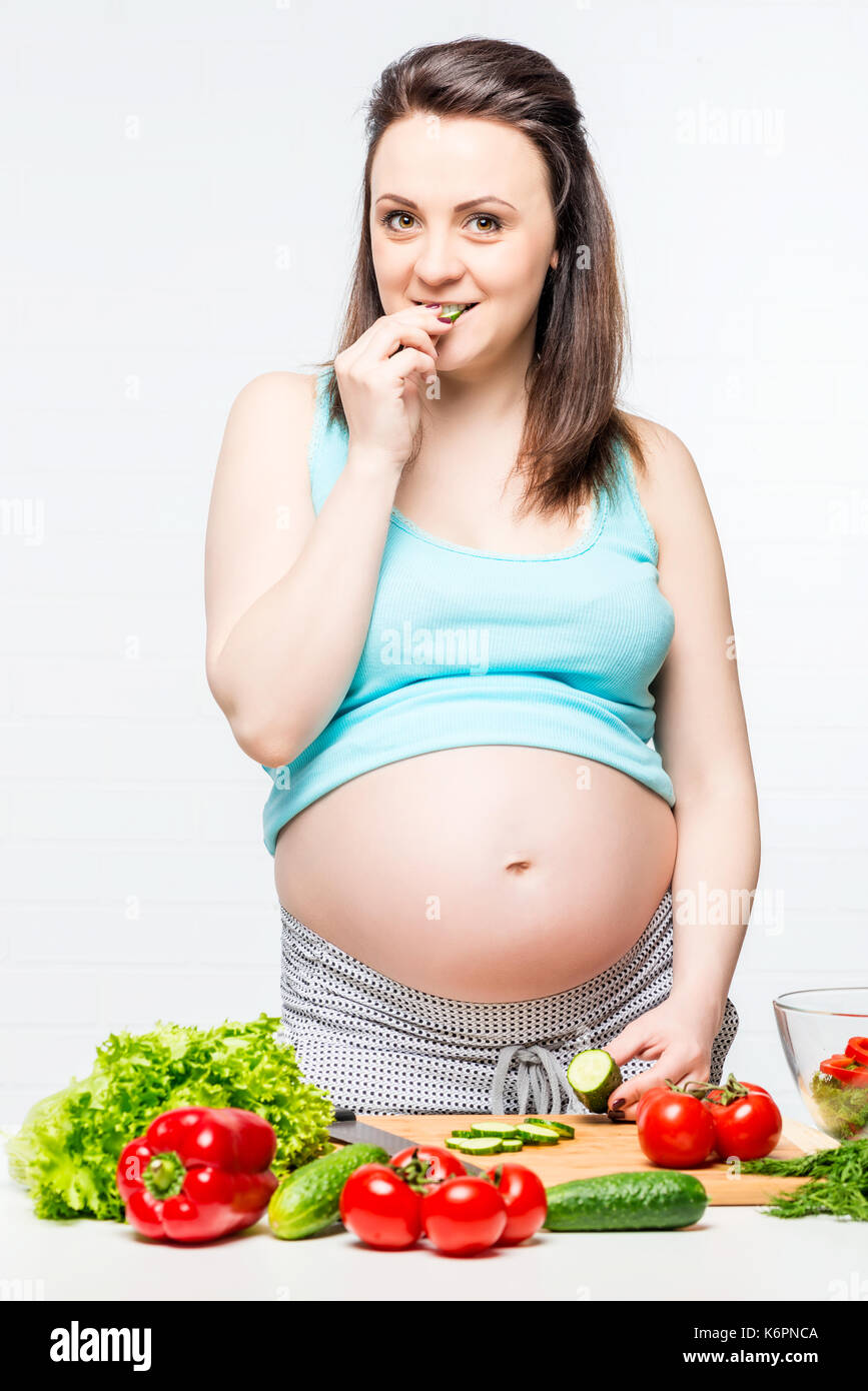 Ragazza con una grande pancia in gravidanza mangiare un cetriolo Foto Stock
