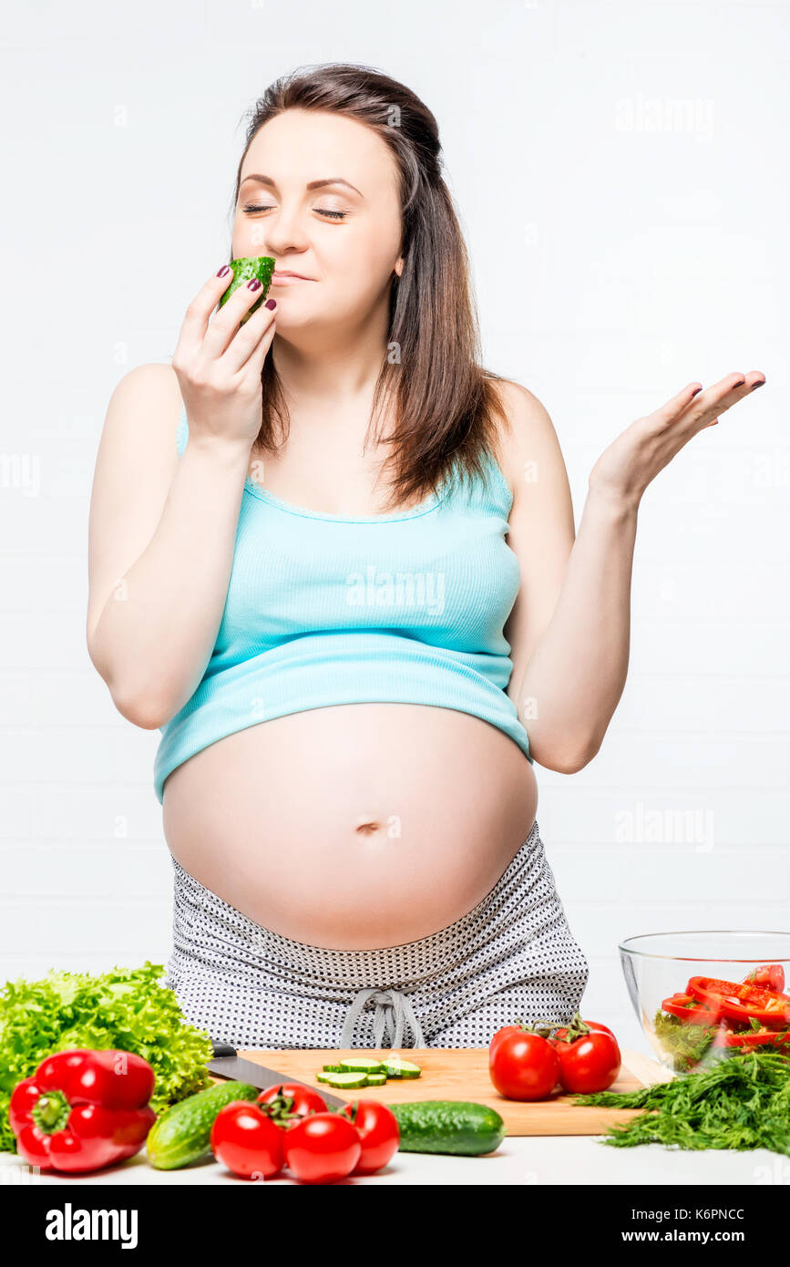 Felice donna incinta con le verdure sul tavolo preparare un insalata Foto Stock