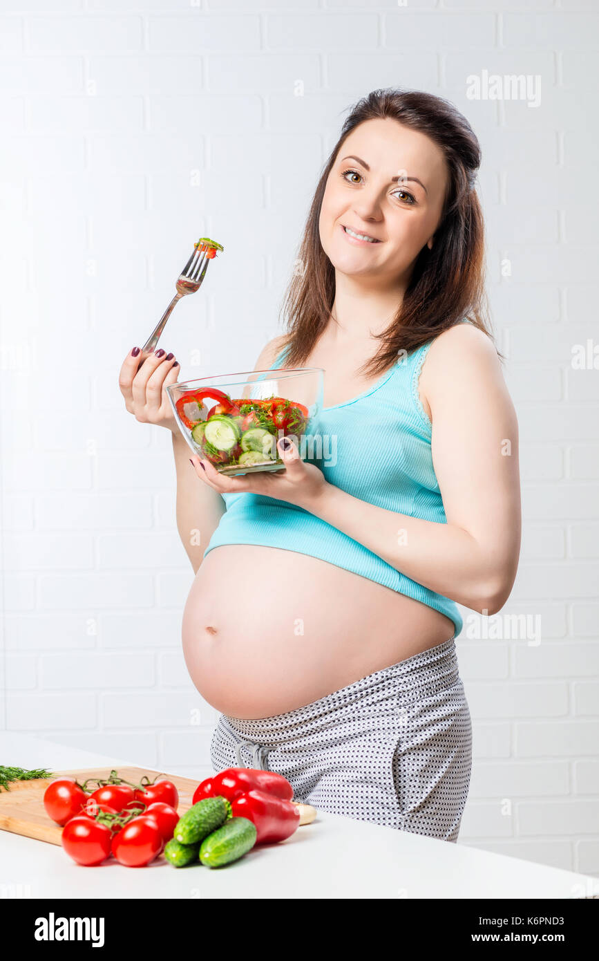 Ritratto verticale di una bella donna incinta con una ciotola di insalata Foto Stock