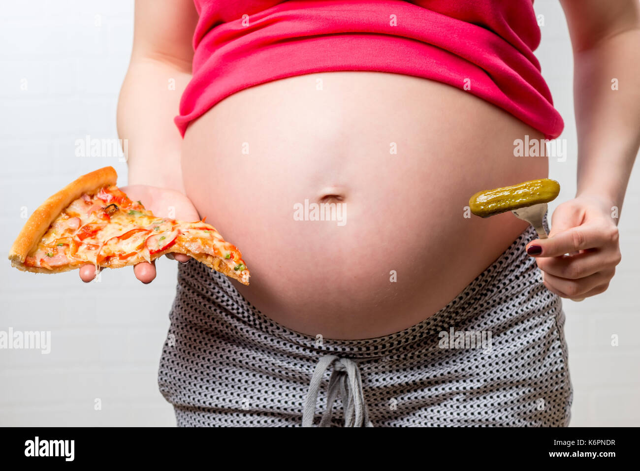 Cibo malsano pizza e salati cetriolo sullo sfondo del ventre di una donna incinta di close-up Foto Stock