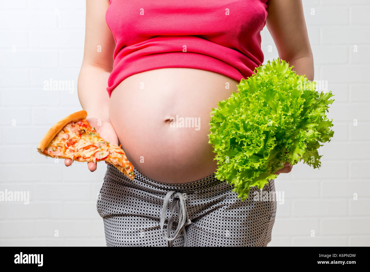 Foto concettuale - inutile e cibo sano nelle mani di una donna in stato di gravidanza su un stomaco closeup sfondo Foto Stock
