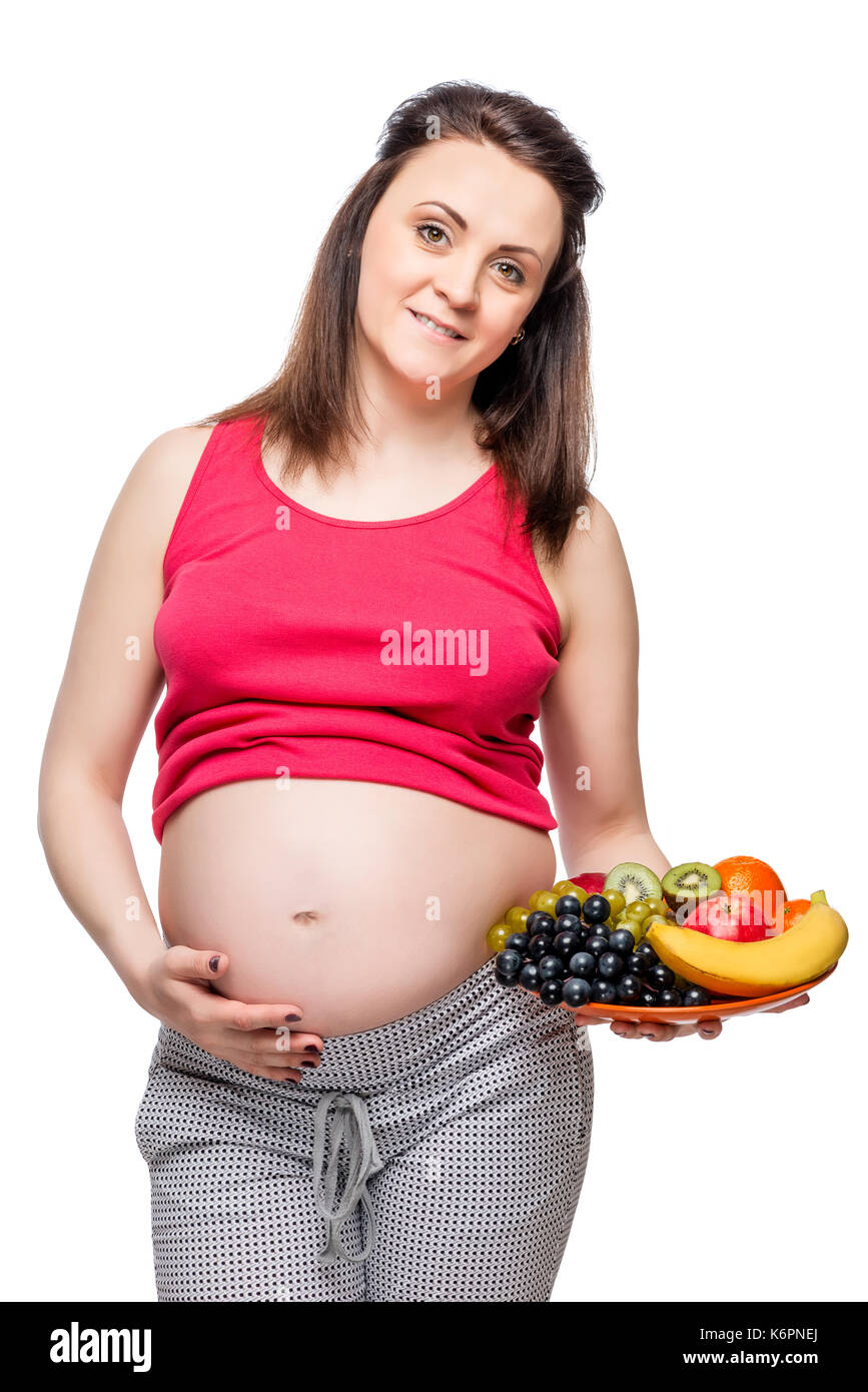 Ritratto di una donna incinta con un piatto di frutta su uno sfondo bianco isolato Foto Stock