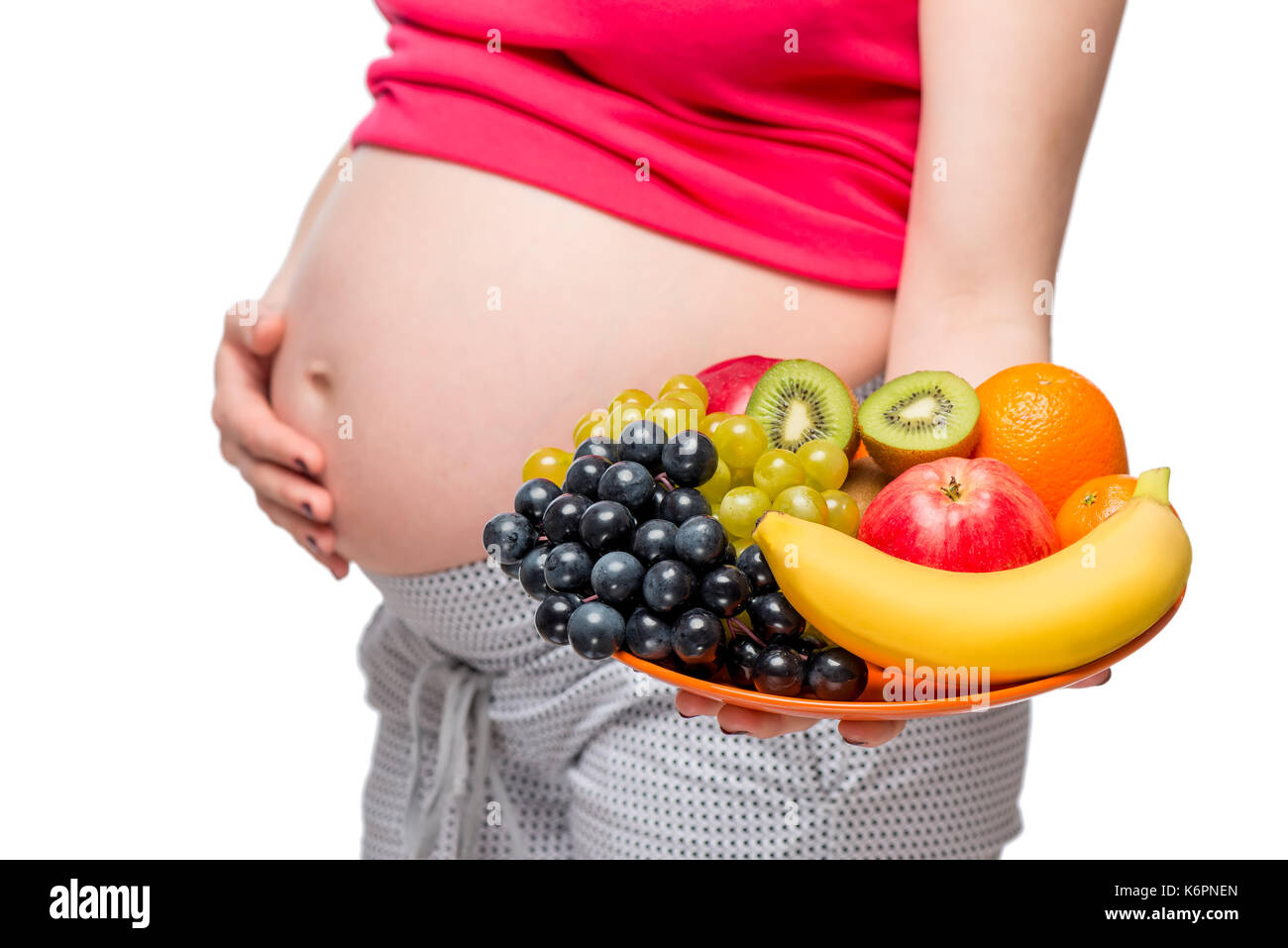 Un piatto di frutta sullo sfondo del ventre di una donna incinta di close-up isolato Foto Stock