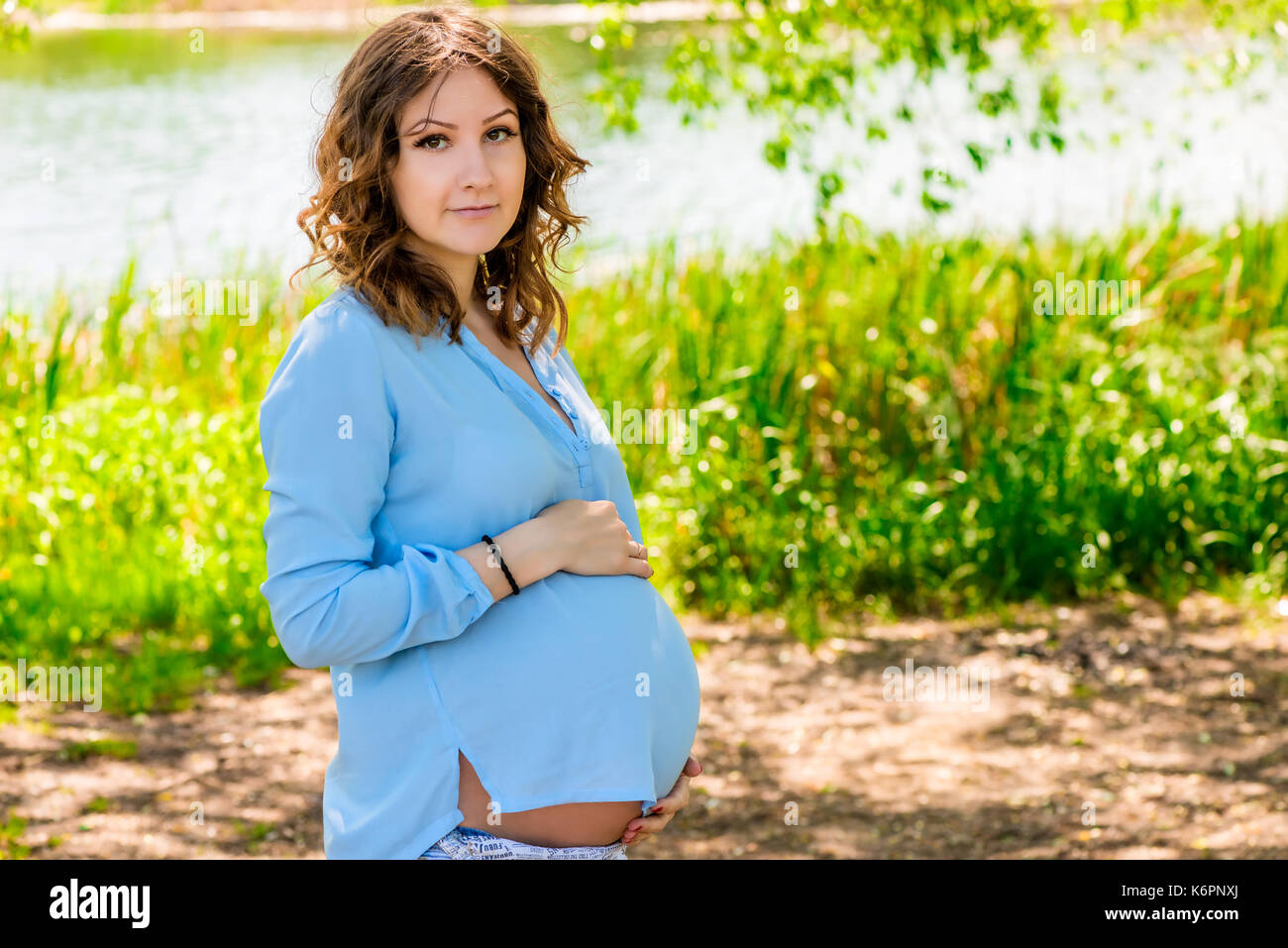 Giovane e bella ragazza incinta in un parco nei pressi di un lago Foto Stock