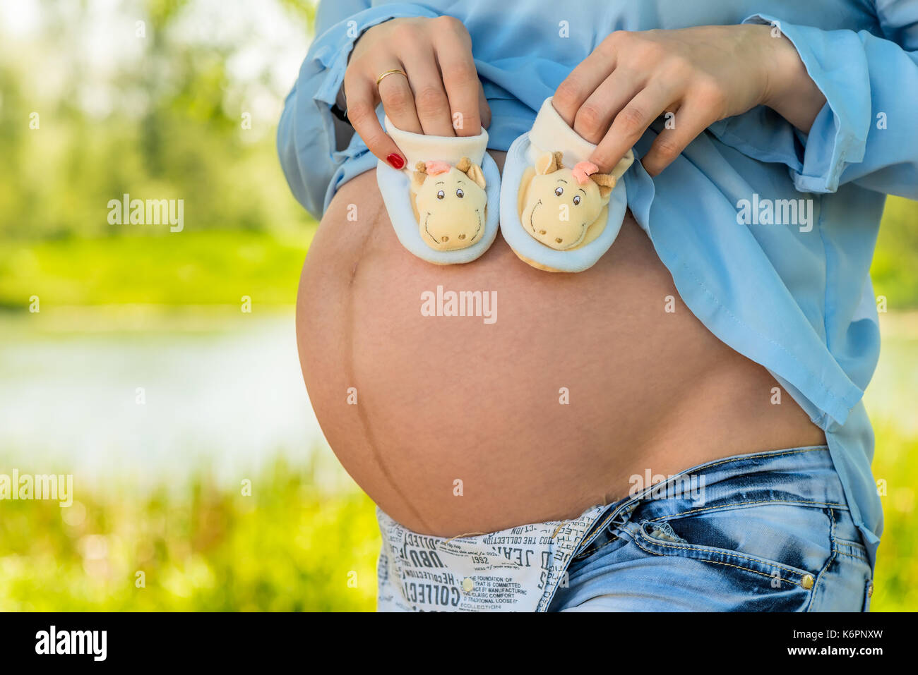 La pancia di una donna incinta di close-up e stivaletti in mani Foto Stock