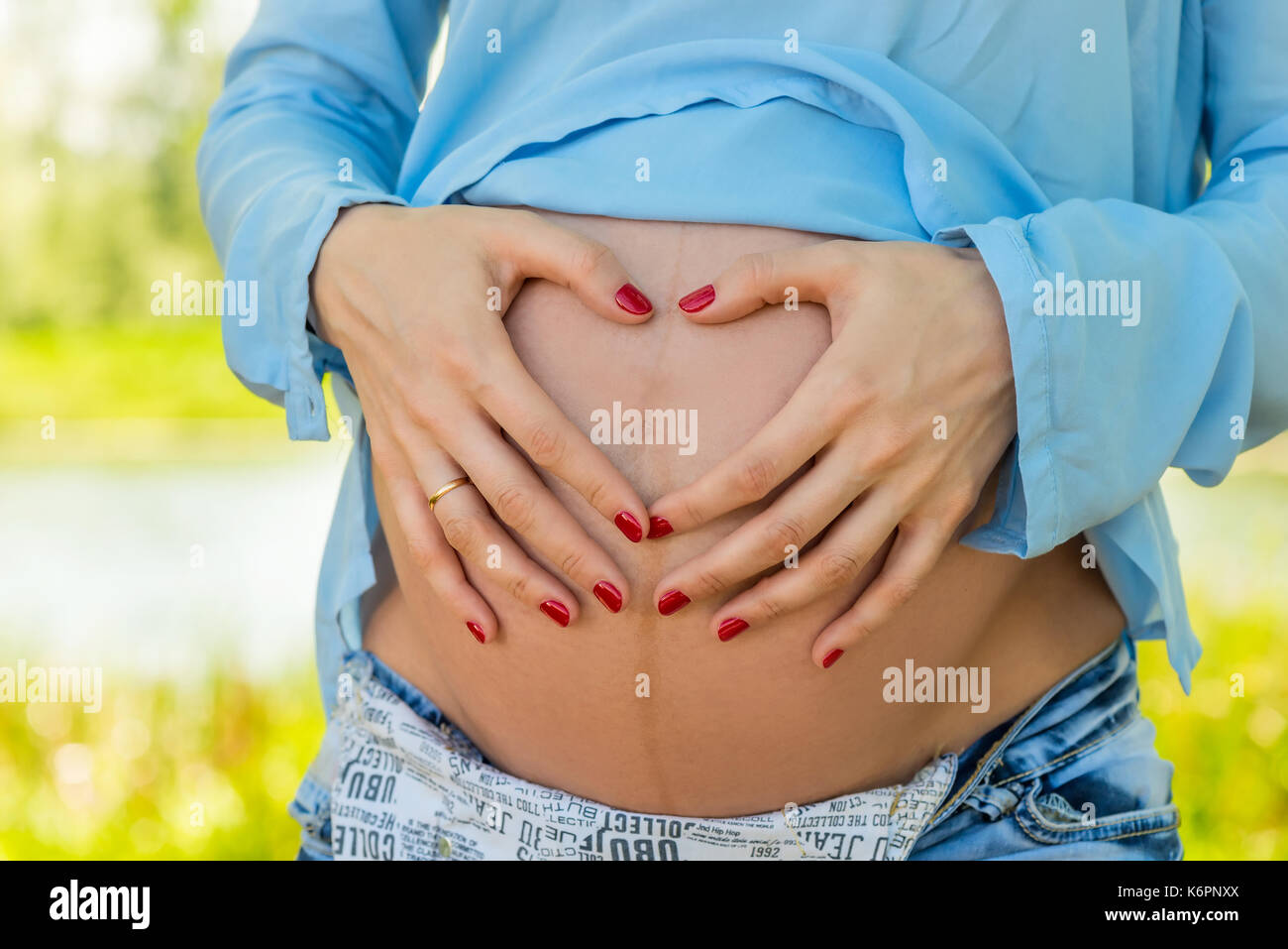 Le mani a forma di cuore sul ventre di una donna incinta di close-up Foto Stock