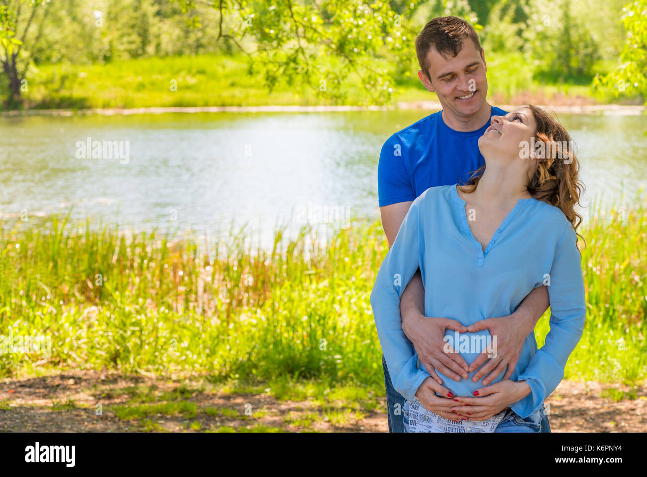 Donna incinta e suo marito in un parco vicino all'acqua avvolgente Foto Stock