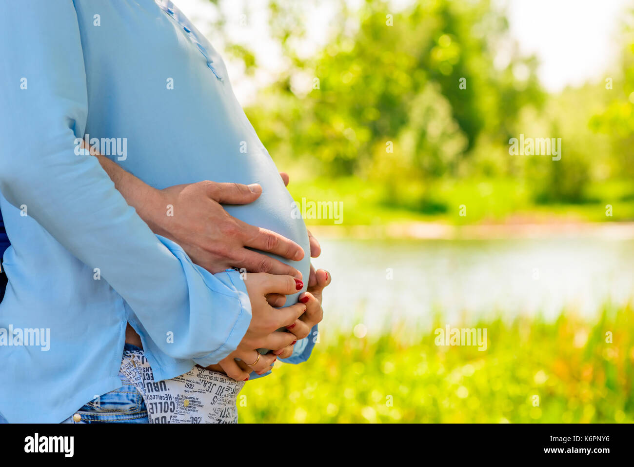 La pancia di una donna incinta abbracciato da un lago nel parco Foto Stock