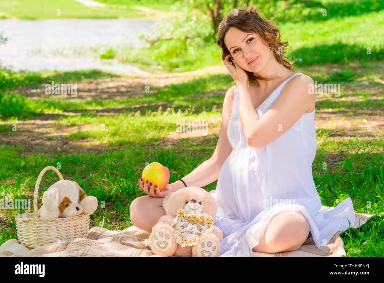 Giovane ragazza incinta in un bianco sarafan su un plaid in un parco a un picnic Foto Stock