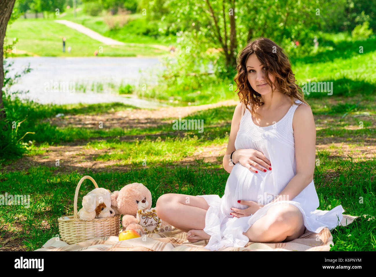 Incinta donna bella in bianche vesti in appoggio su un picnic nel parco Foto Stock