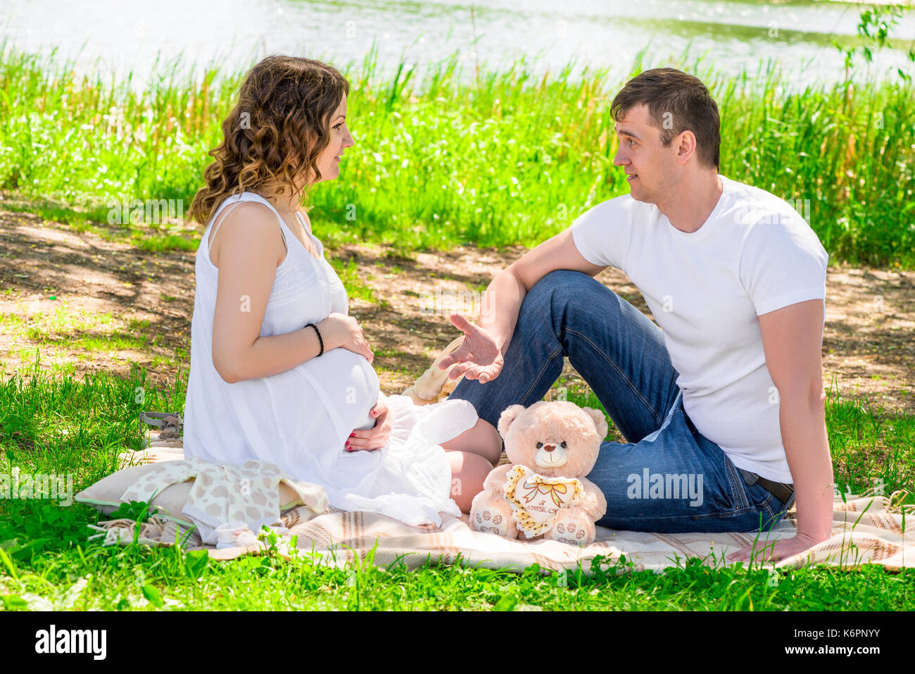 L'uomo e sua moglie incinta in appoggio su un picnic in un parco vicino al lago Foto Stock