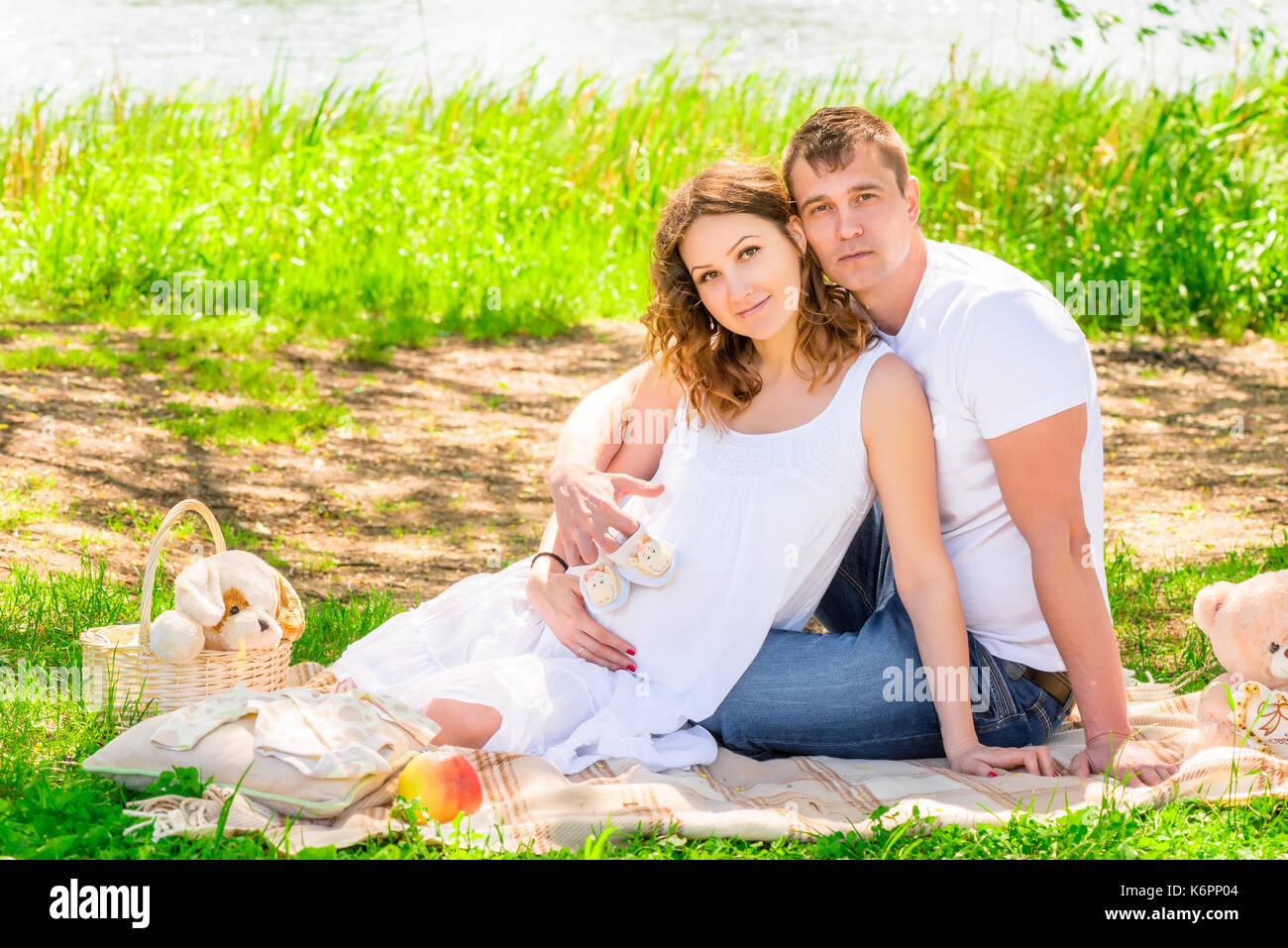 Pic-nic nei pressi del lago, giovane coppia incinta su un plaid Foto Stock