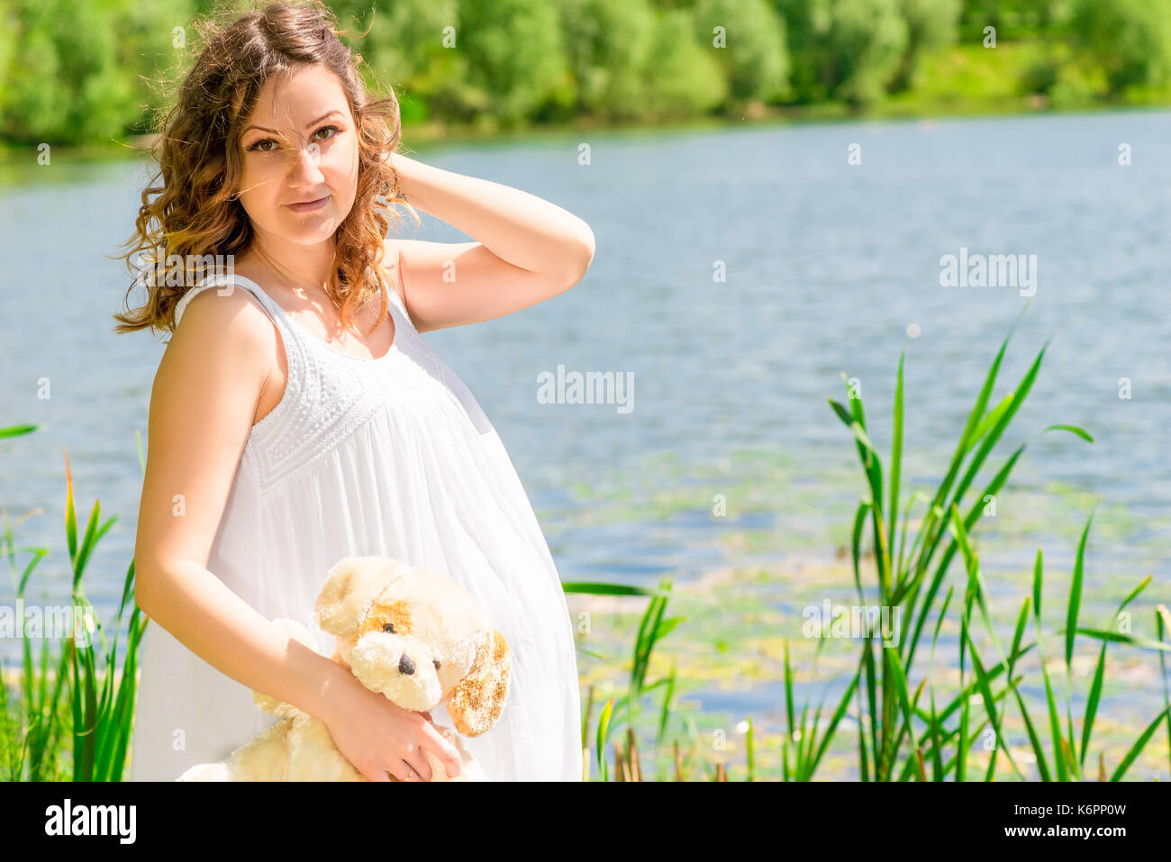 Ritratto orizzontale di una donna in stato di gravidanza in un bianco sarafan vicino a un lago Foto Stock