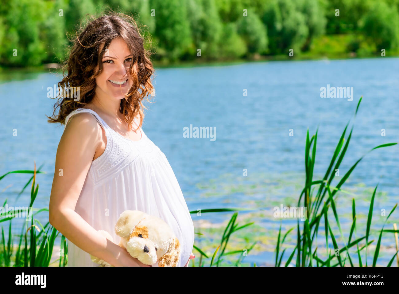Carina ragazza incinta sullo sfondo di un bellissimo lago nel parco in posa Foto Stock